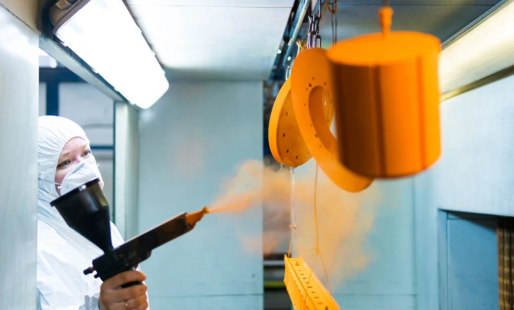 This image depicts an electrostatic powder coating booth, capturing an operator in the process of applying powder to a component.